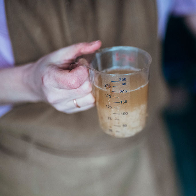 Hand holding a measuring cup with liquid in beverage production or brewing facility