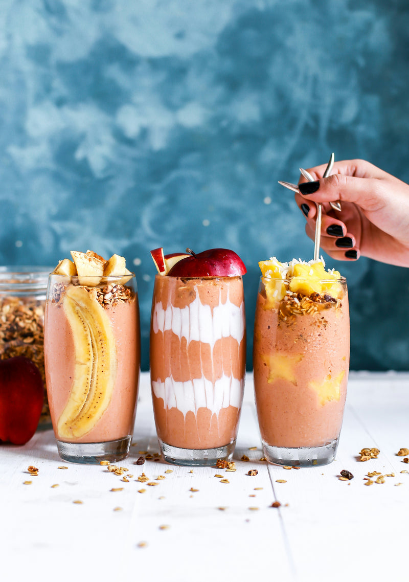 Three colorful fruit smoothies with fresh toppings arranged on a white surface against a vibrant blue background - healthy beverages