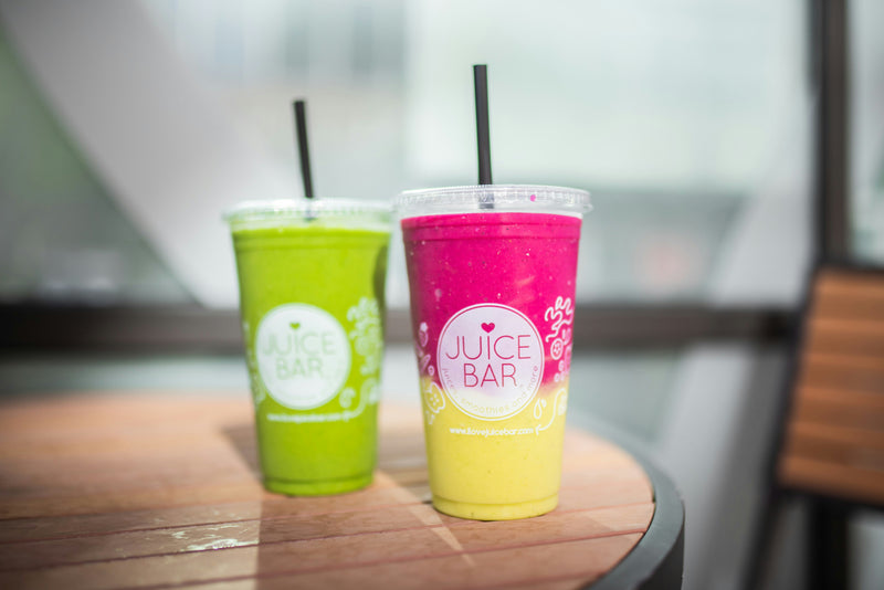 Two vibrant colorful smoothie cups from a juice bar displayed on a rustic wooden table