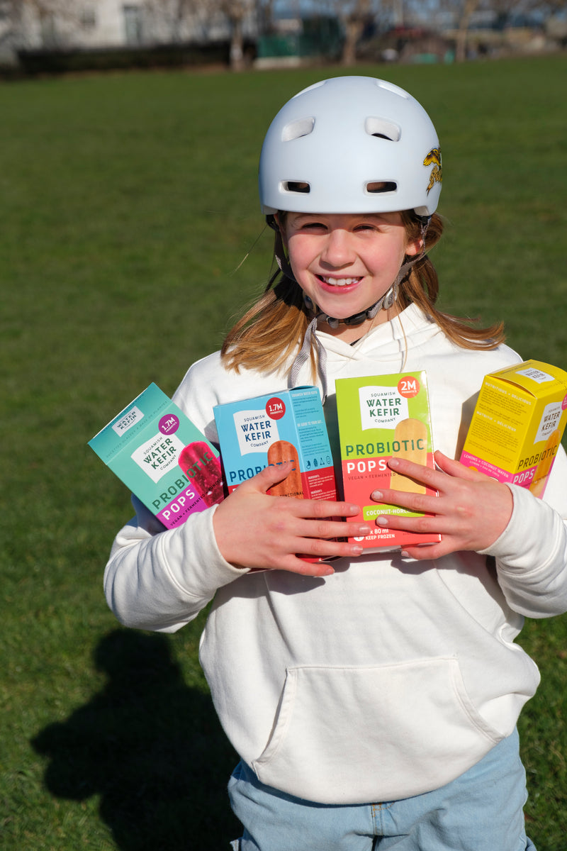 Child wearing a helmet holding probiotic product boxes on grass