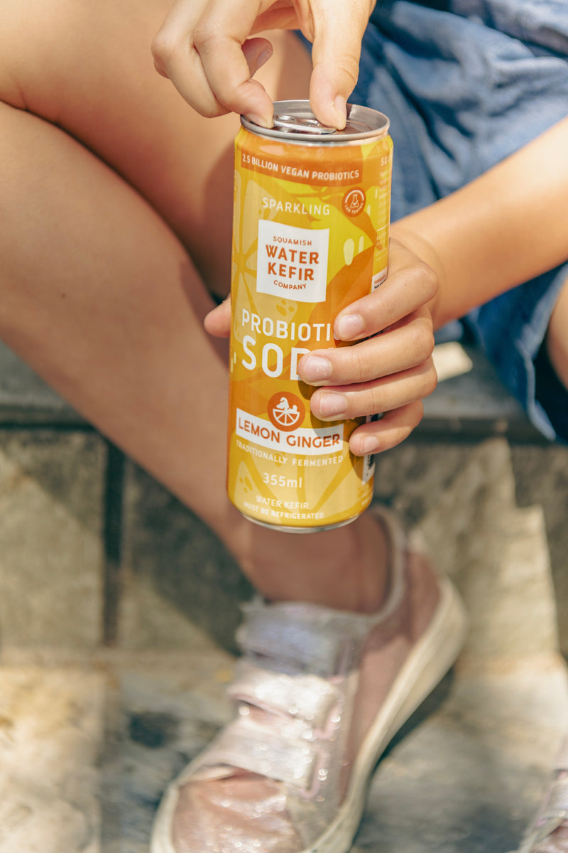 Person holding a can of probiotic soda with lemon ginger flavor outdoors