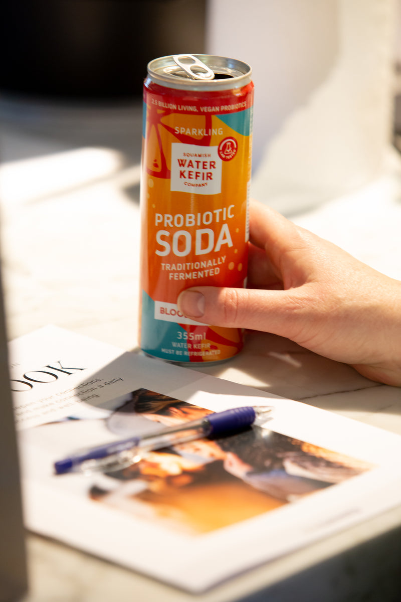 Hand holding a can of probiotic soda displayed on a magazine with pen