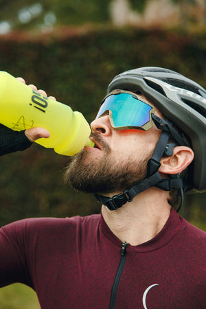 Man in cycling gear drinking water from a yellow sports bottle outdoors - active cyclist hydration