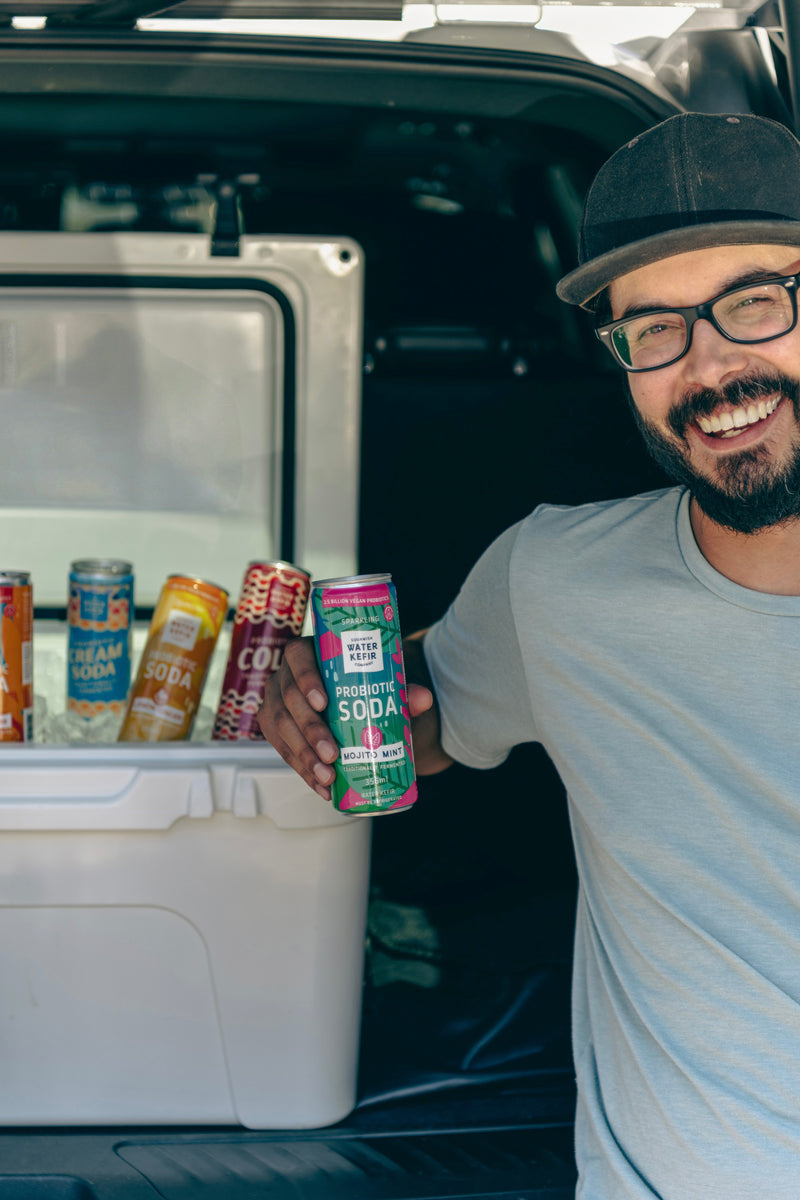 Man holding a can of soda in front of an open car trunk with a cooler full of drinks