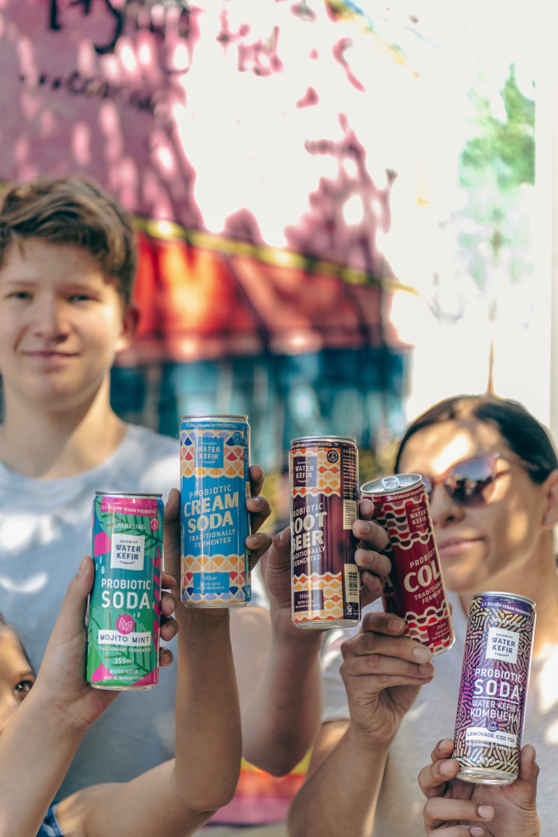 People holding various Squamish Water Kefir cans with colorful labels outdoors