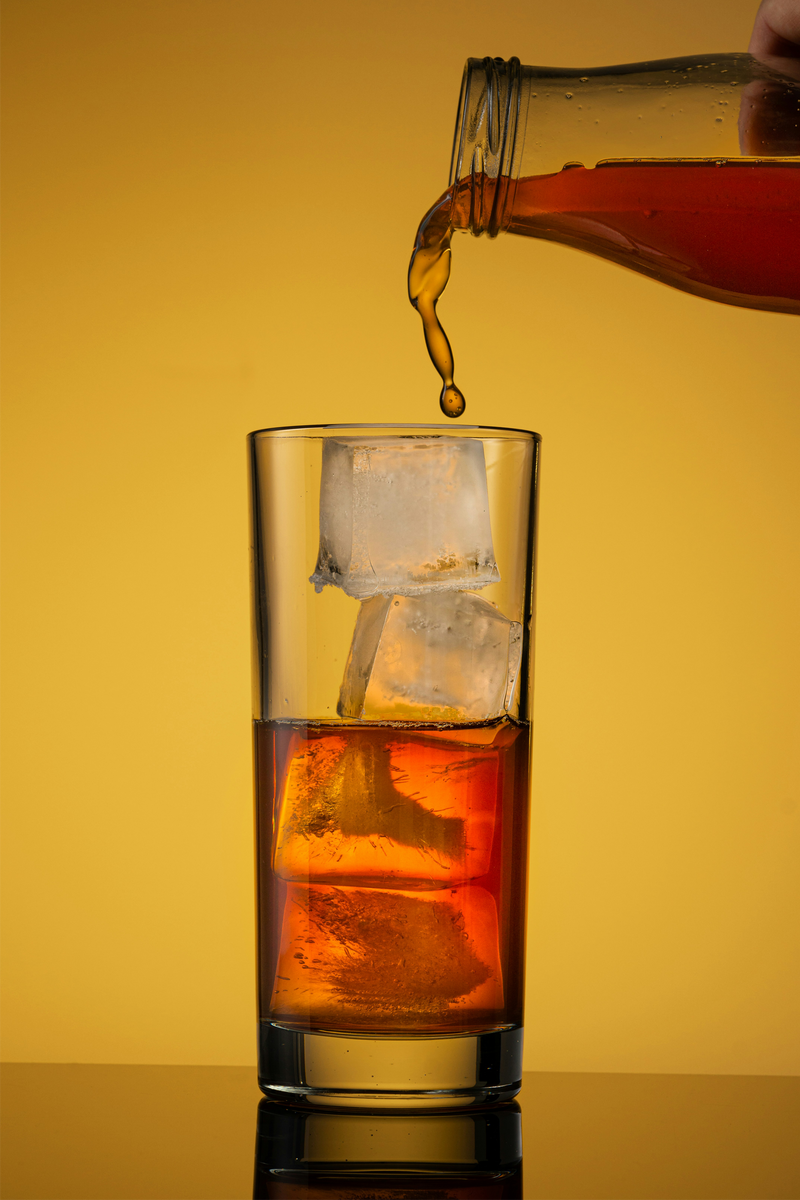 Glass of refreshing iced tea being poured from a pitcher against a vibrant yellow background